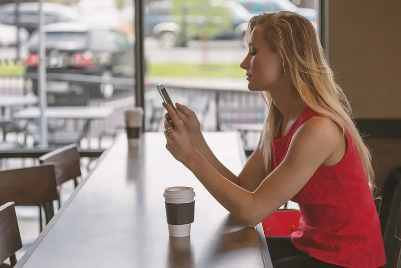 eine Frau, die eine Nachricht auf einem Smartphone liest, während sie an der Theke sitzt