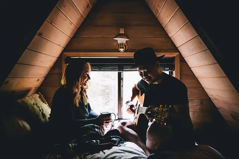 Eine Frau hört ihrem Freund zu, wie er auf dem Bett Gitarre spielt