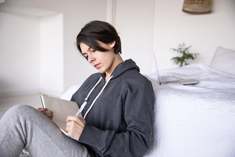 eine Frau, die in ein Notizbuch schreibt, während sie neben dem Bett sitzt