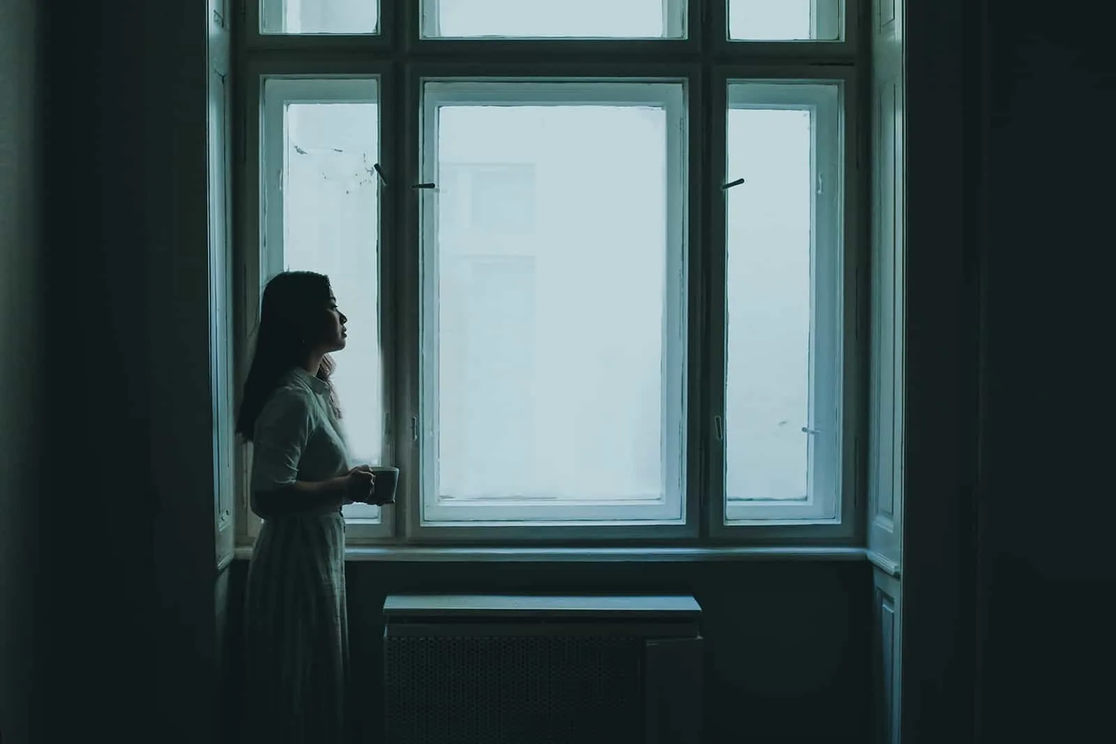 eine Frau, die in einem dunklen Raum neben dem Fenster steht