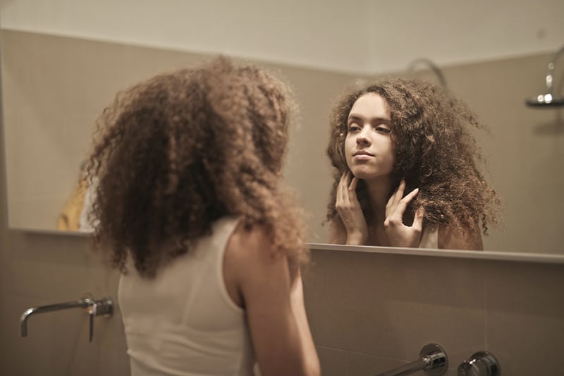 eine Frau, die sich in den Spiegel schaut und ihre Haare berührt