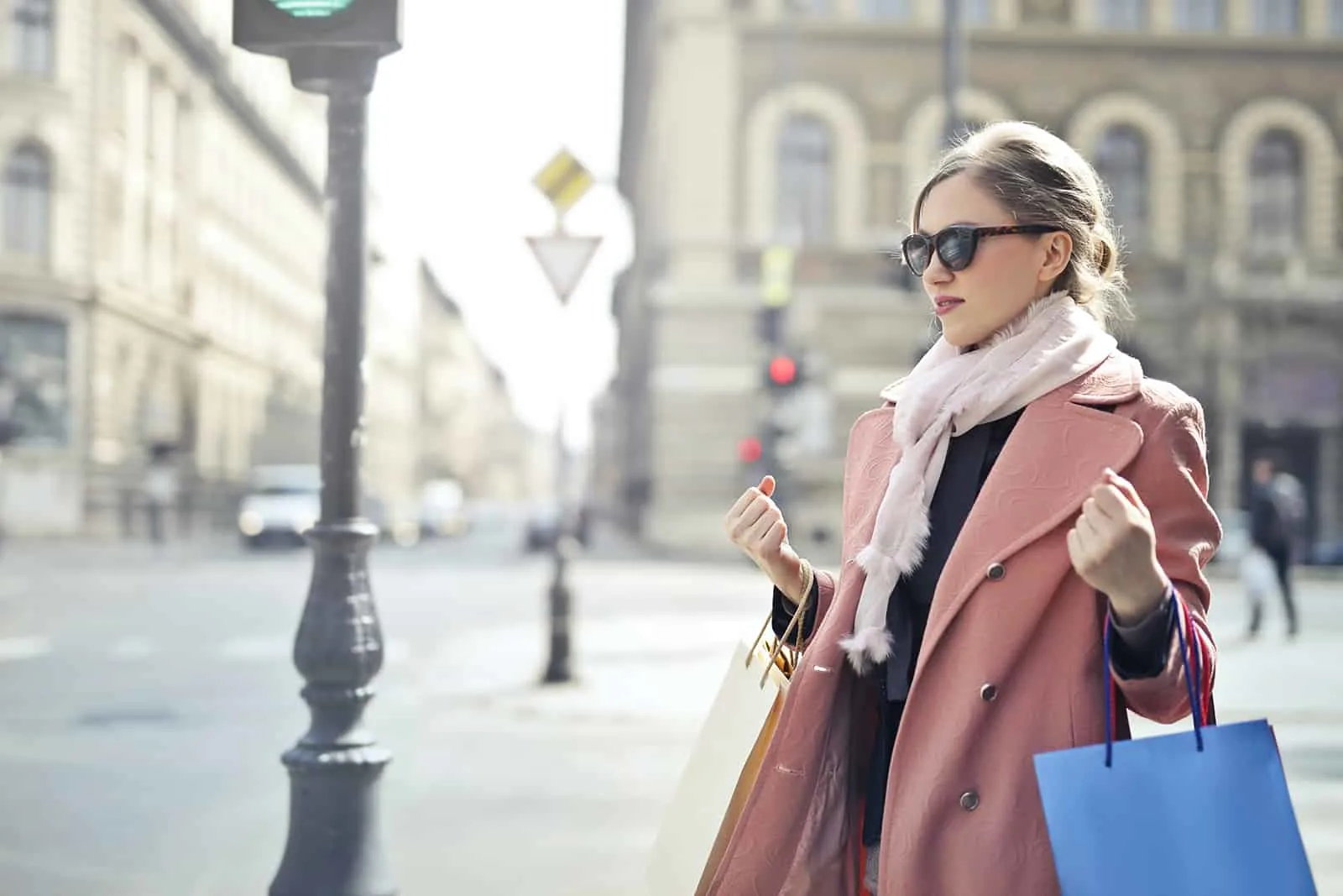 eine Frau in einem rosa Mantel, der Einkaufstaschen hält, die auf dem Bürgersteig stehen