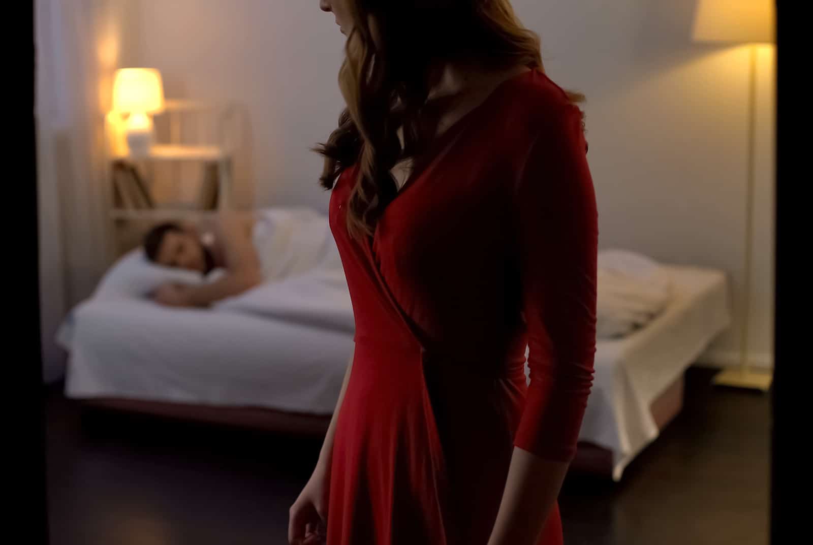 eine Frau in einem roten Kleid verlässt den Raum, während ein Mann in einem Bett schläft