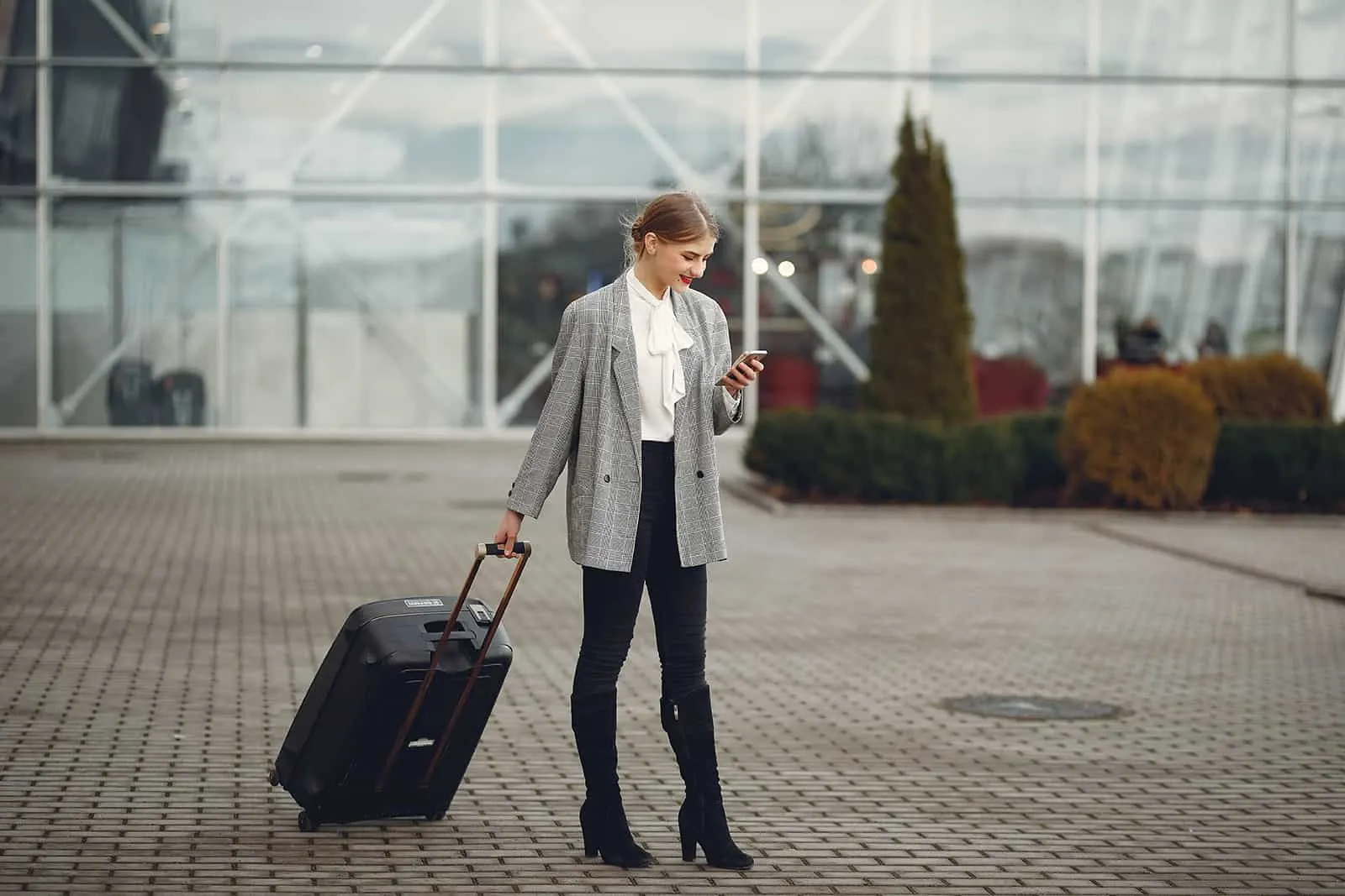 eine Frau mit einem Koffer SMS auf einem Smartphone vor dem Flughafen stehen