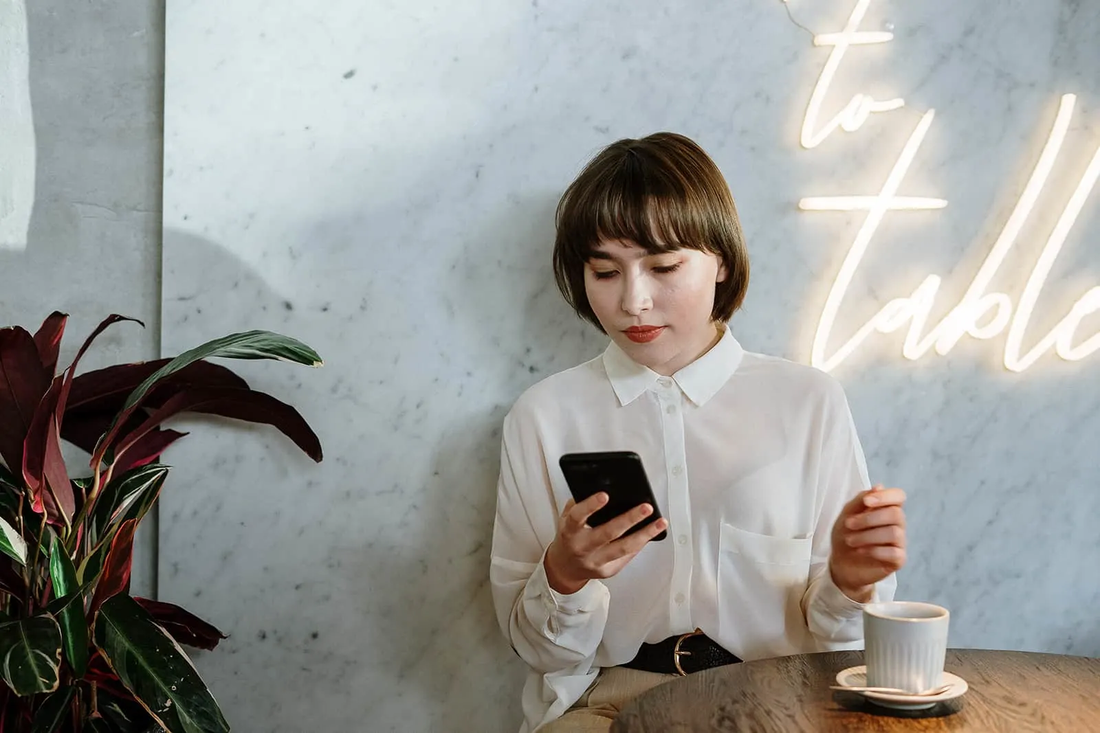 eine Frau, die ein Smartphone benutzt, während sie alleine in einem Café sitzt