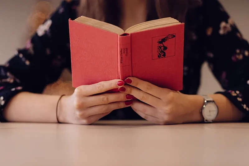eine Frau, die ein rotes Buch hält, während sie am Tisch sitzt