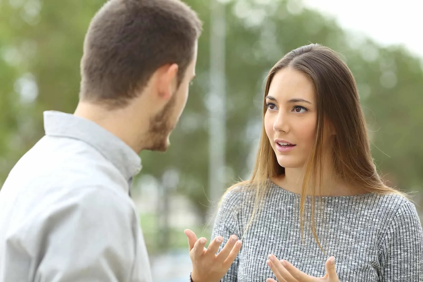 Eine Frau mit langen braunen Haaren spricht mit einem Mann, während sie draußen draußen steht