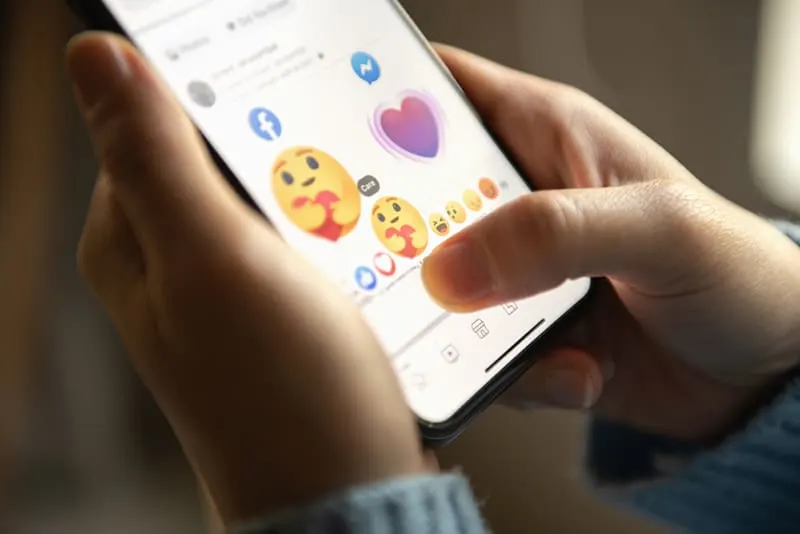 Eine Person, die Emoji auf dem Smartphone auswählt, während sie Facebook nutzt