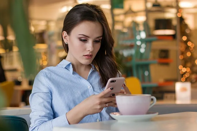 eine ernsthafte Frau, die auf ihr Smartphone schaut, während sie im Café sitzt
