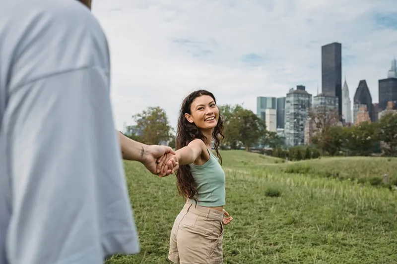 eine lächelnde Frau, die die Hand ihres Freundes hält, während sie im Park geht