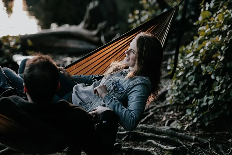 eine lächelnde Frau, die in einer Hängematte mit einem Mann im Wald liegt