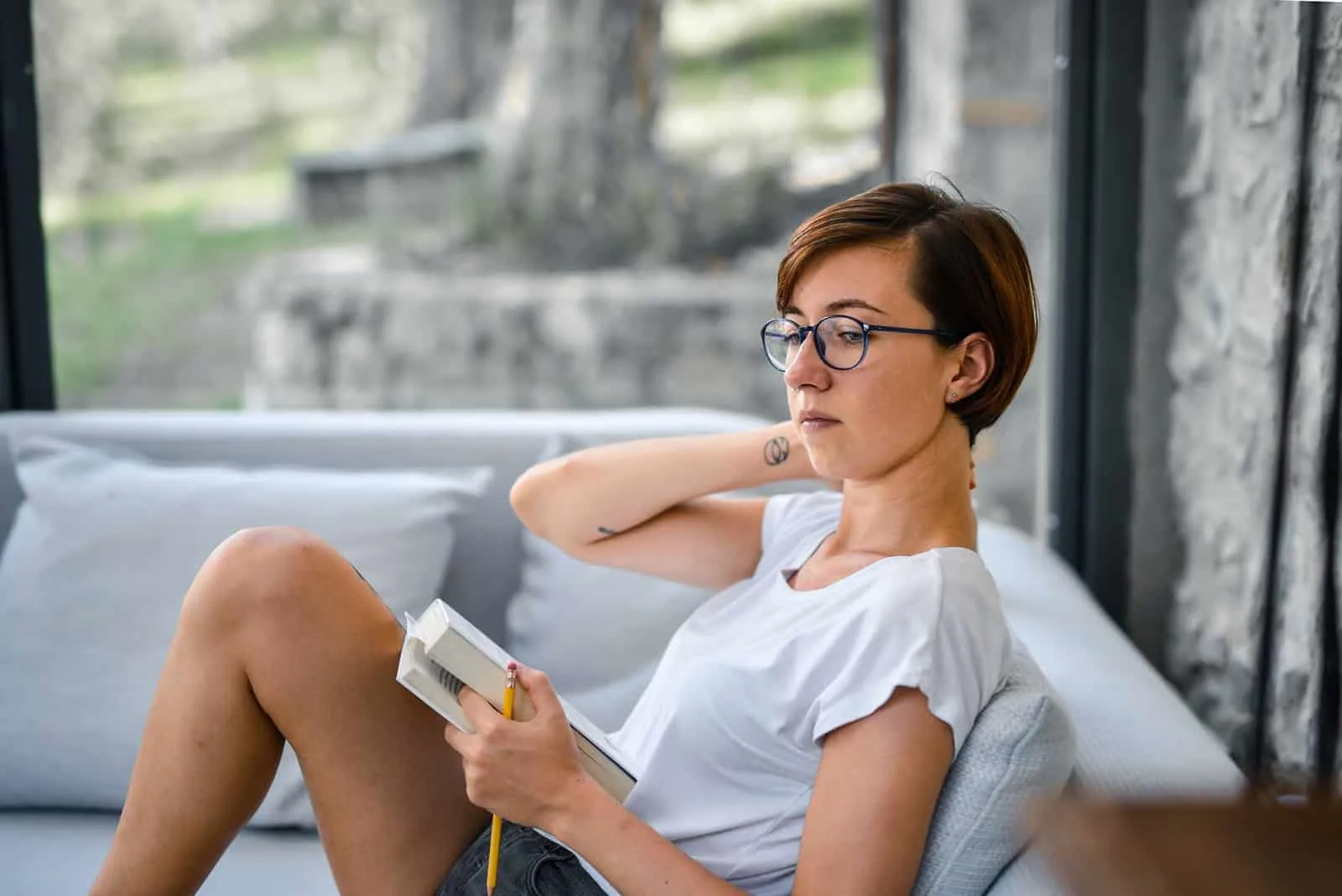 eine nachdenkliche Frau, die ein Buch hält, während sie auf dem Sofa sitzt