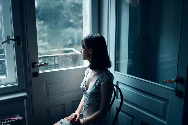 eine nachdenkliche Frau, die auf dem Stuhl sitzt und durch das Fenster schaut
