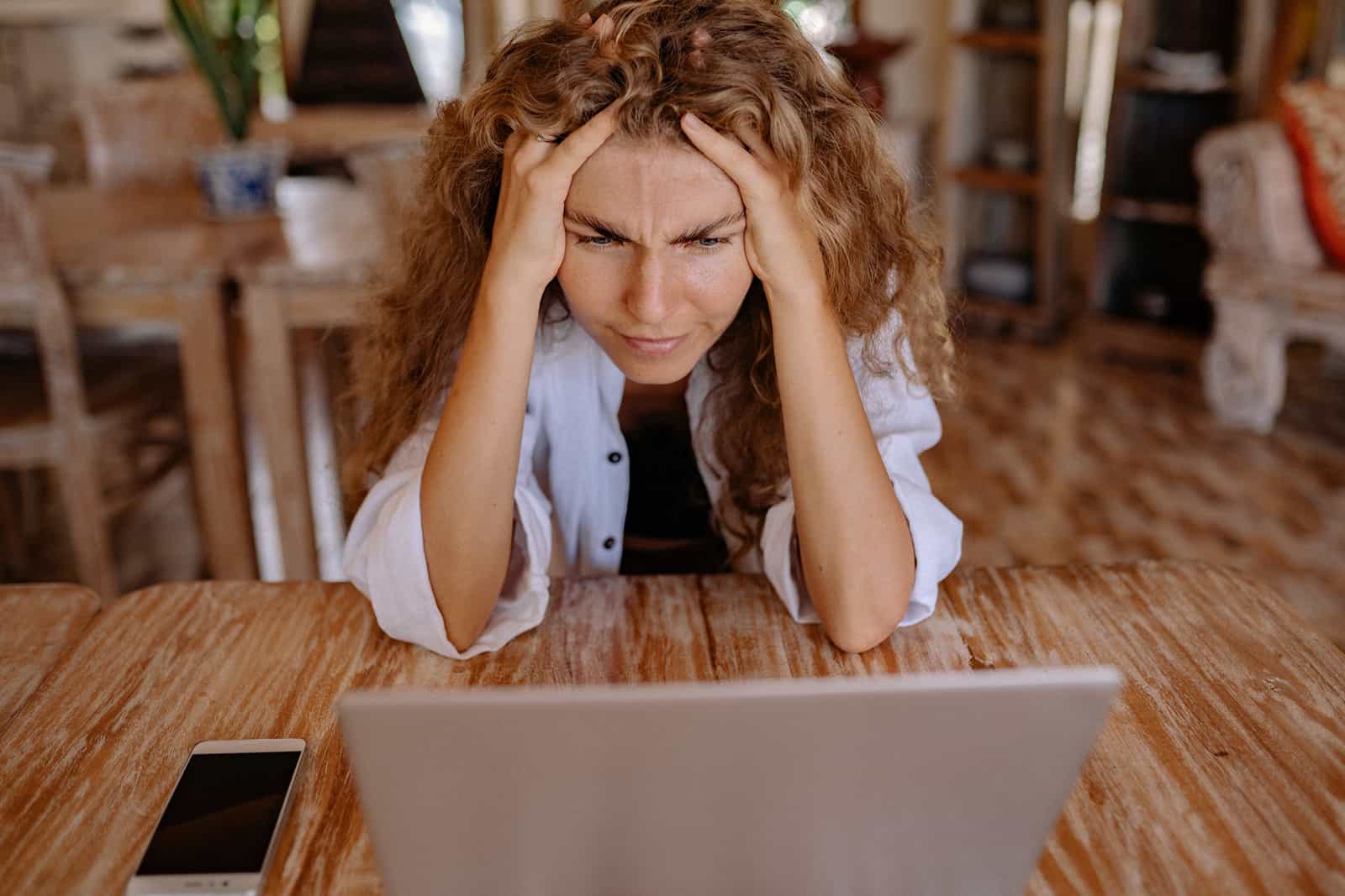 eine nervöse Frau, die vor dem Laptop sitzt und den Kopf mit den Händen berührt