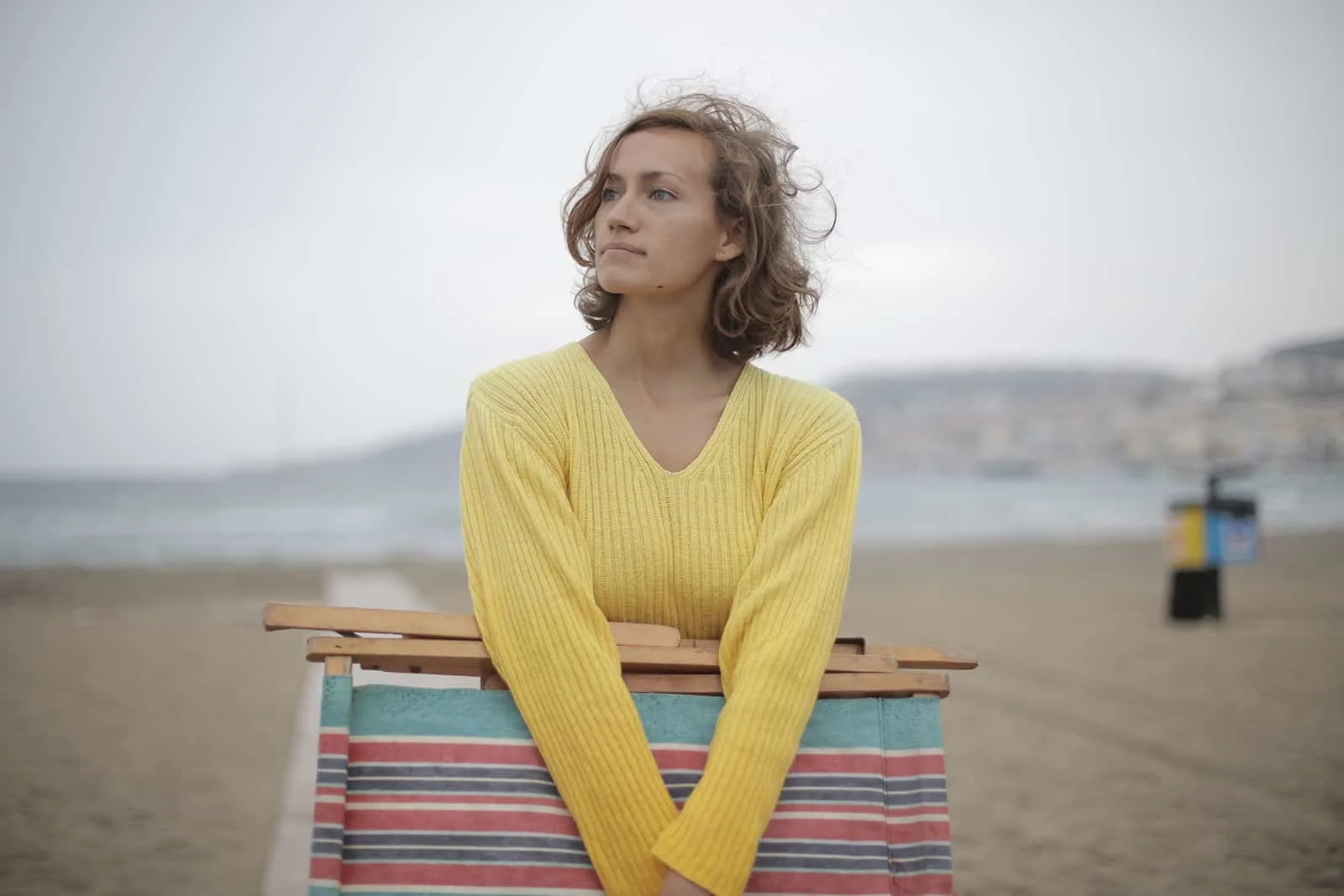 eine ruhige Frau, die einen gefalteten Liegestuhl hält, während sie am Strand steht