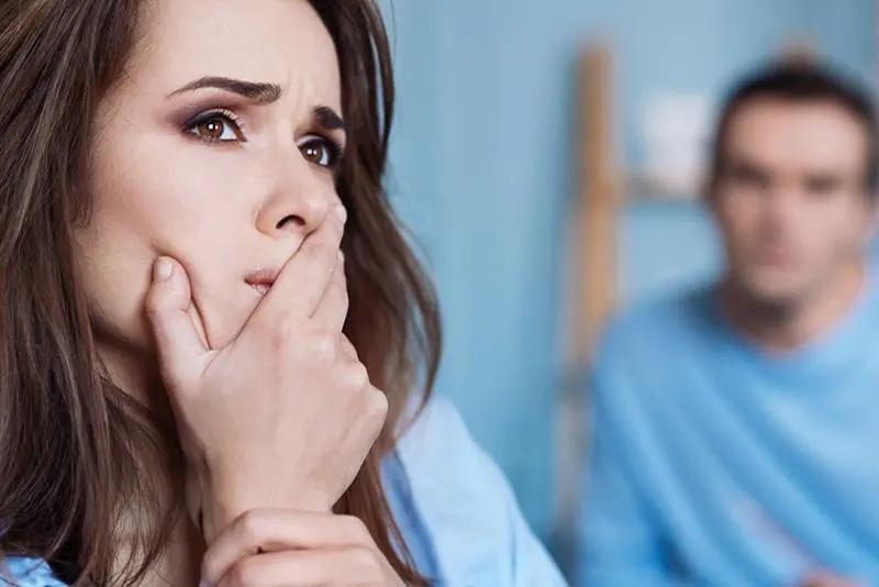 enttäuschte Frau, die ihren Mund mit einer Handfläche bedeckt, während sie den Kopf von ihrem Freund abwendet