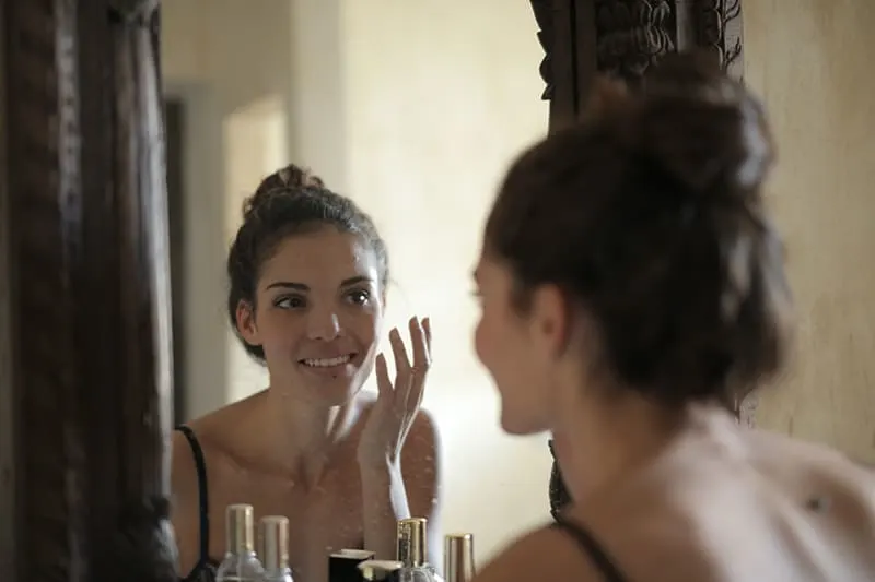 glückliche Frau, die vor dem Spiegel steht, während Creme aufträgt