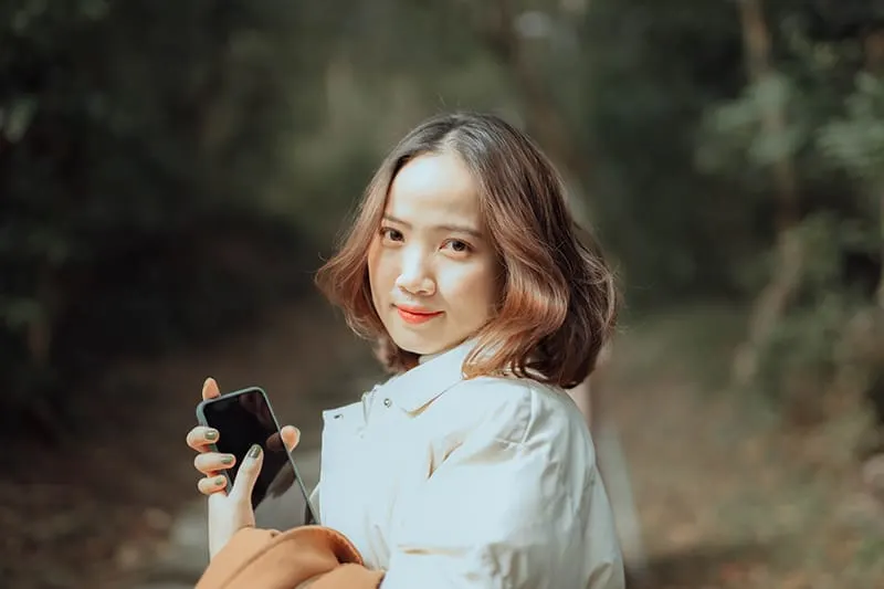lächelnde Frau, die Smartphone hält, während sie im Park steht