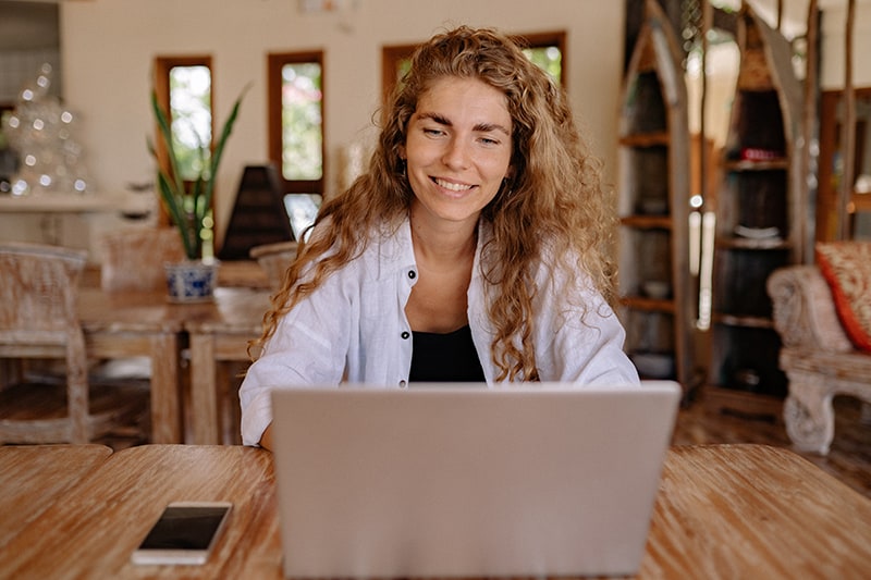 lächelnde Frau, die auf ihrem Laptop plaudert, während sie am Tisch sitzt