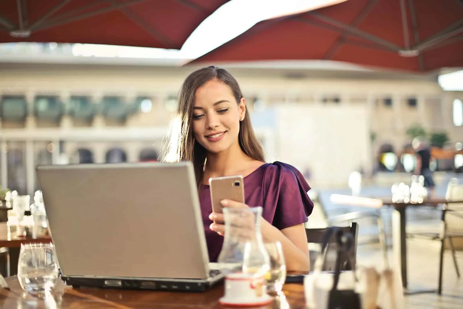 lächelnde Frau, die eine Nachricht auf ihrem Smartphone liest, das im Café sitzt