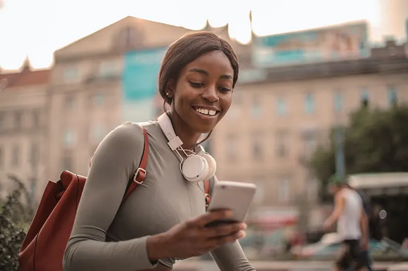 lächelnde Frau, die ihr Smartphone beim Gehen in der Stadt betrachtet