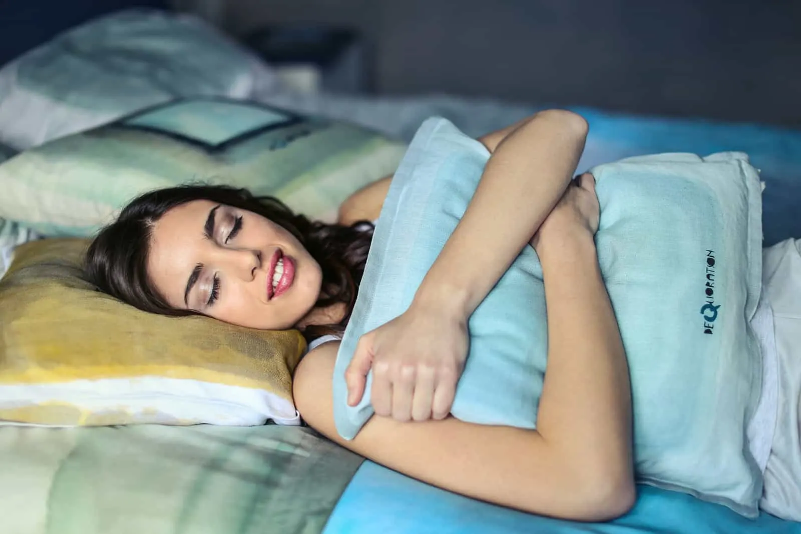 lächelnde Frau mit geschlossenen Augen umarmt ein Kissen, während sie auf einem Bett liegt