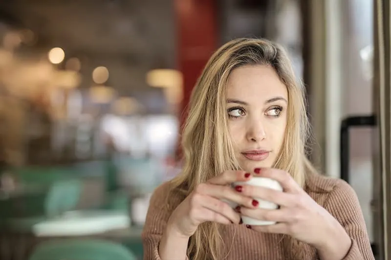nachdenkliche Frau hält Tasse Kaffee und schaut zur Seite
