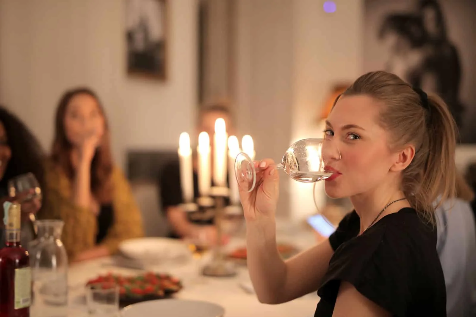 positive Frau, die Wein während eines Abendessens mit Freunden trinkt