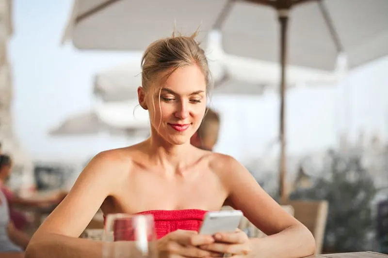 positive Frau, die ihr Smartphone beim Sitzen im Café betrachtet