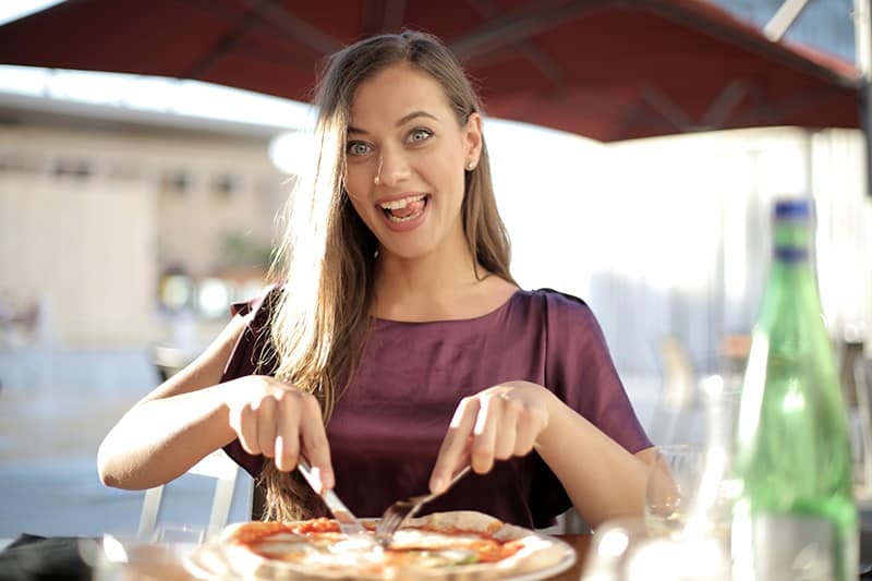 positive Frau, die eine Pizza im Restaurant schneidet
