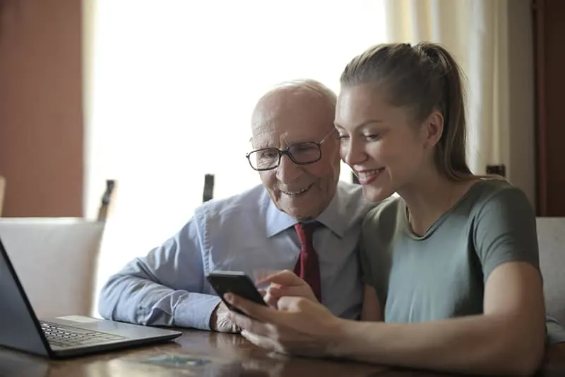 positive Frau, die einem älteren Mann zeigt, wie man ein Smartphone benutzt, während man am Tisch sitzt