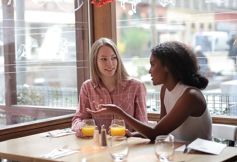 positive blonde Frau im Gespräch mit ihrer Freundin im Café