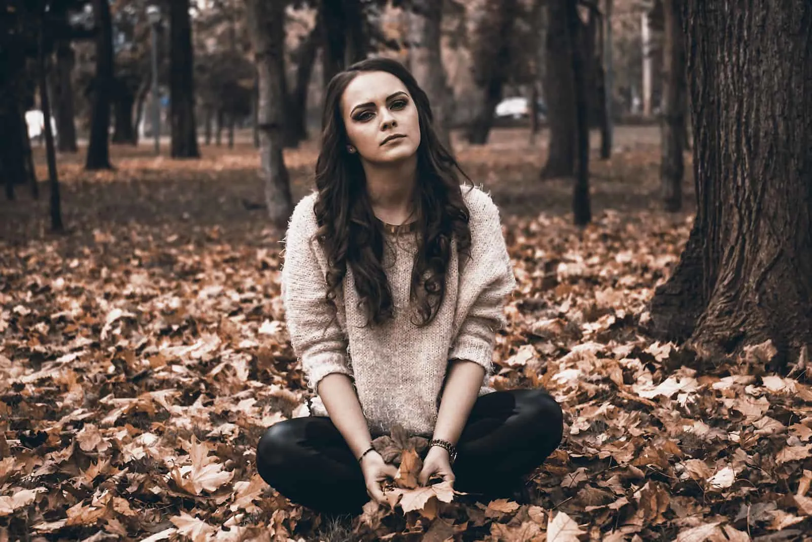 traurige Frau, die auf trockenen Blättern im Park sitzt