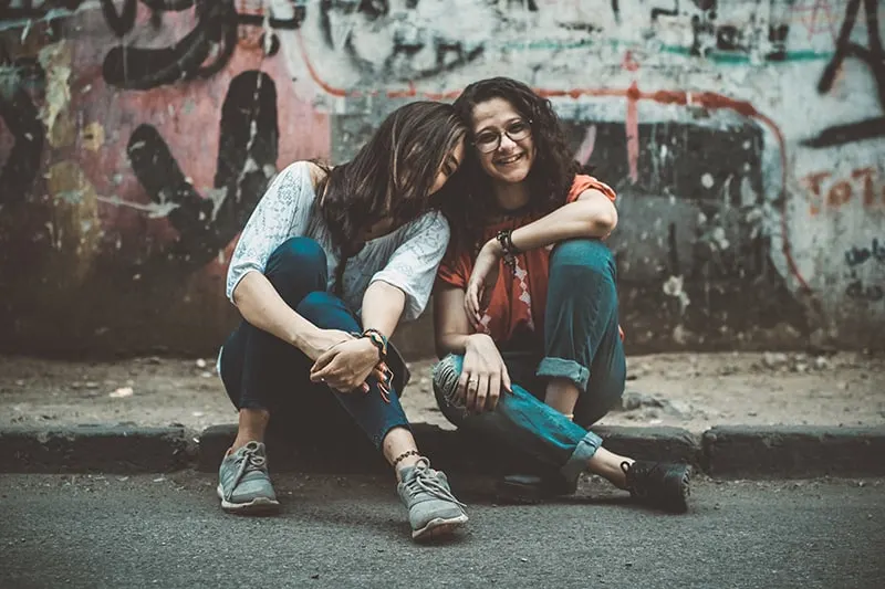 zwei Freundinnen, die sich aufeinander stützen und auf dem Bürgersteig sitzen