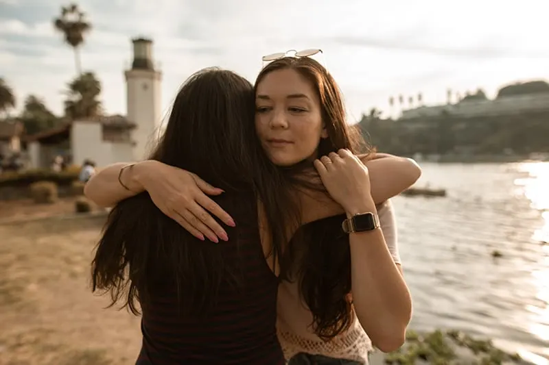 Zwei Freundinnen umarmen sich, während sie in der Nähe des Sees stehen
