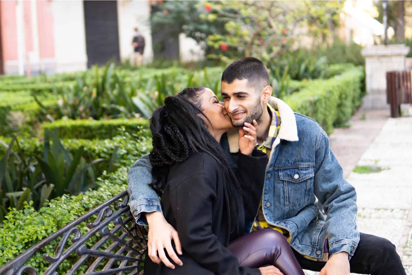 Auf einer Parkbank sitzt ein glückliches Paar in Liebe, das sich umarmt und küsst