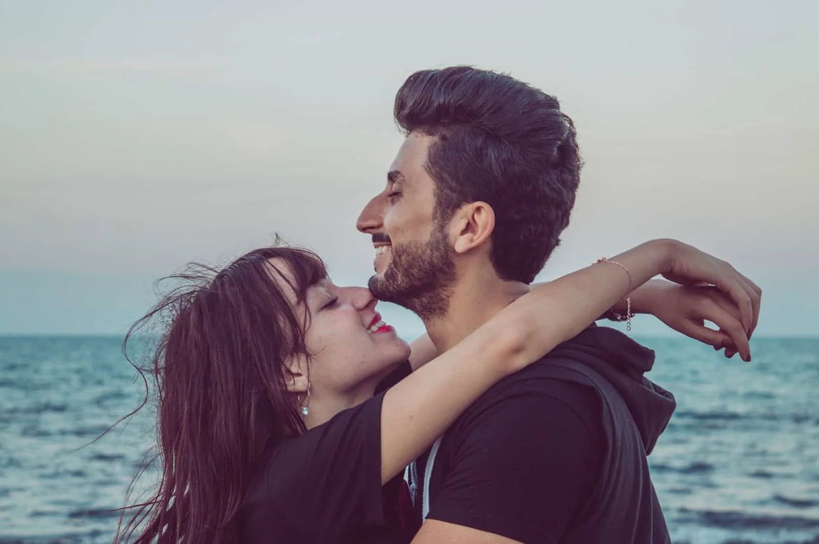 Ein fröhlicher Mann und eine Frau umarmen sich am Meer