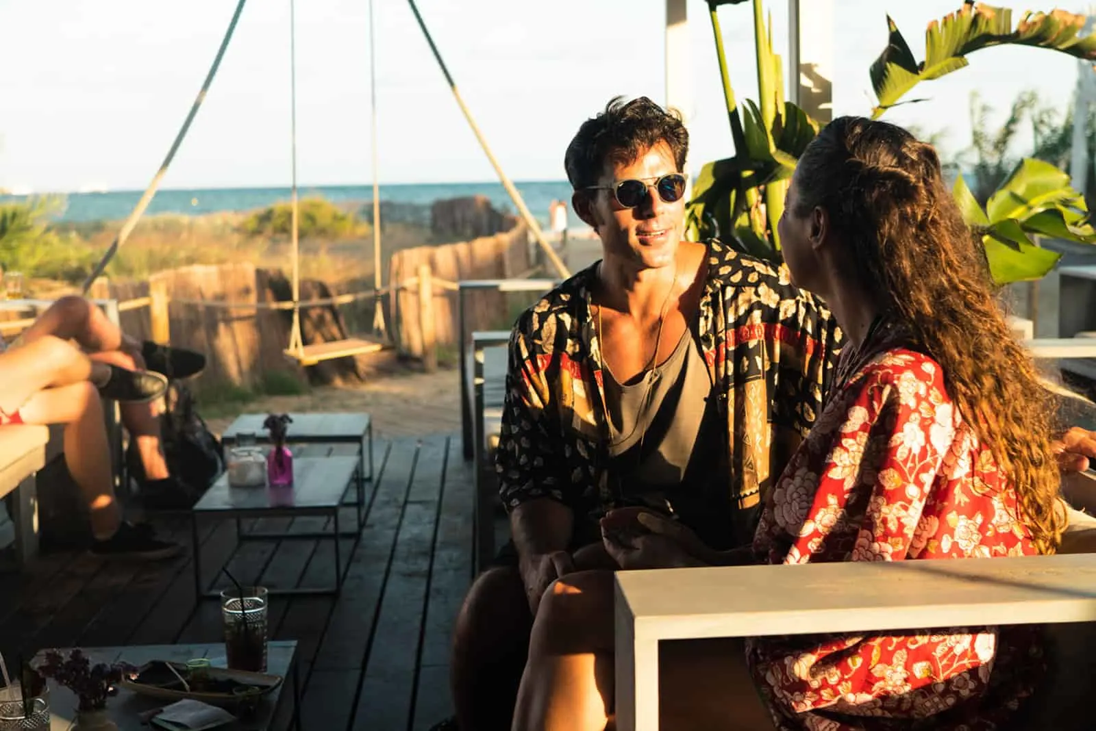 Ein Mann mit Sonnenbrille sitzt mit einer Frau im Café am Strand