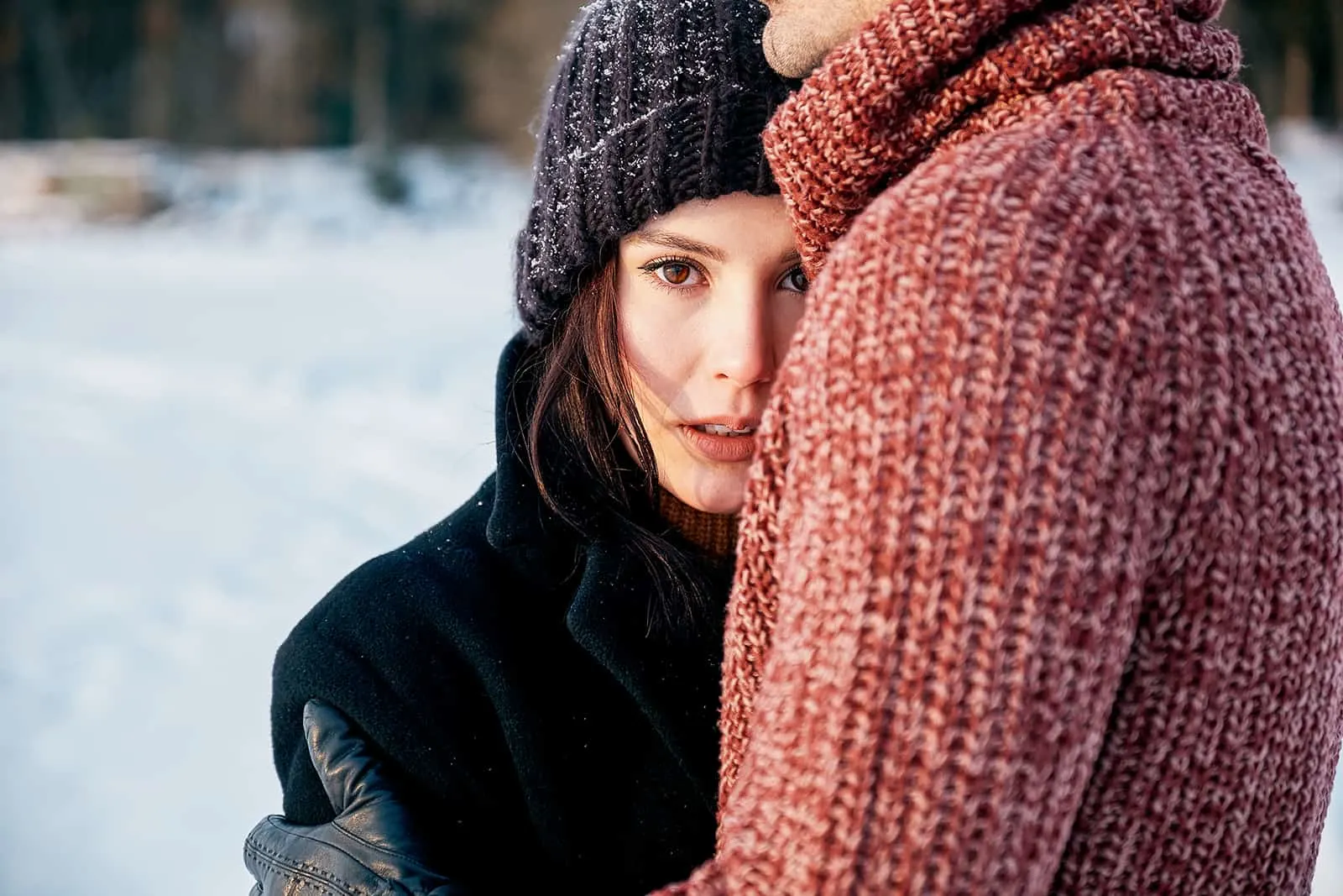 Ein Mann umarmt eine verwirrte Frau, während er auf dem Schnee steht