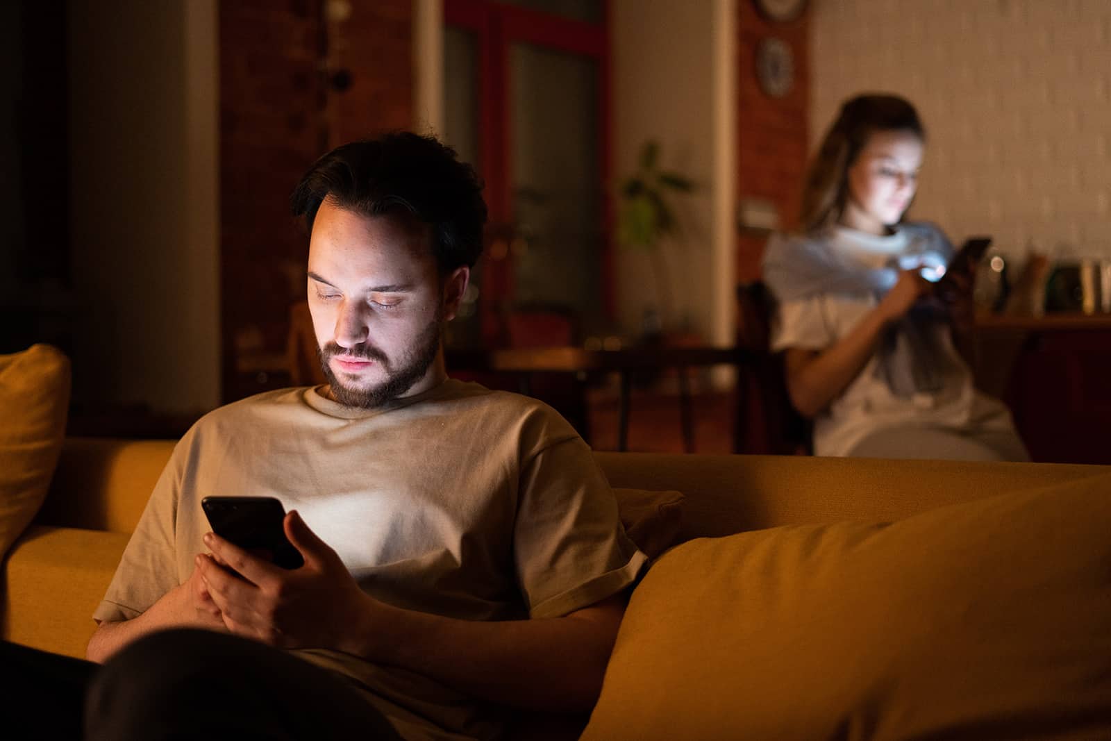 Ein Mann und eine Frau, die ihre Smartphones benutzen, sitzen alleine in getrennten Räumen