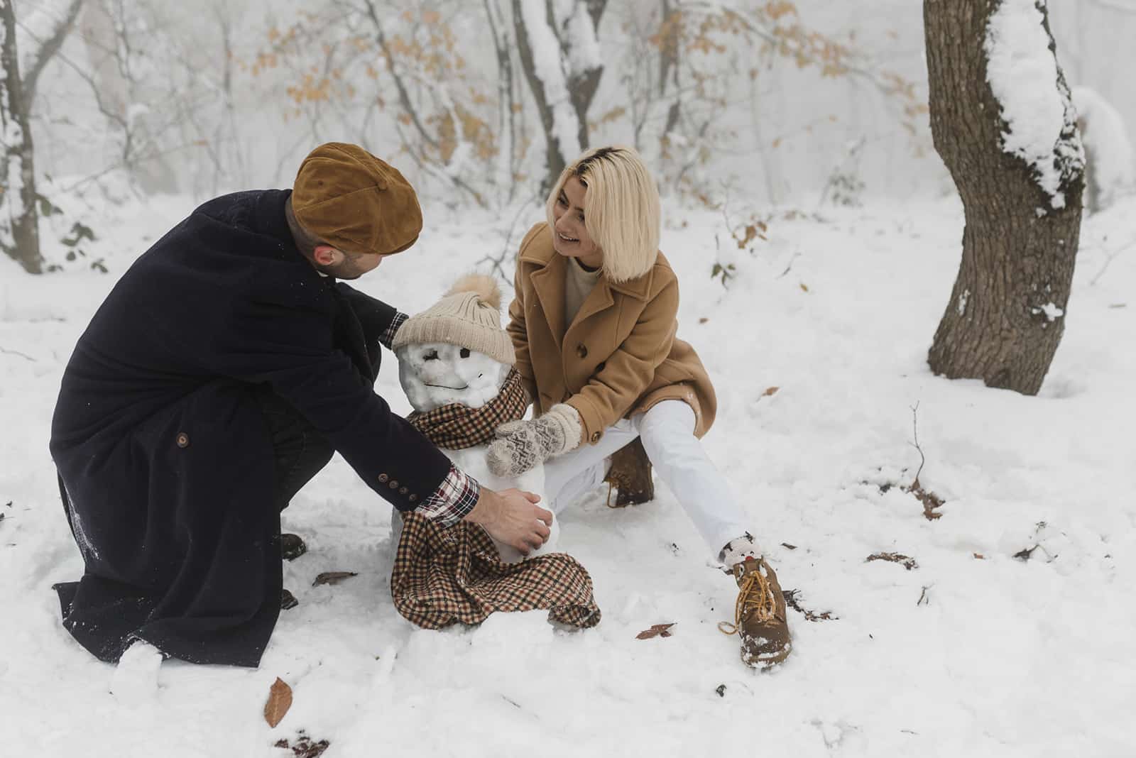 Ein Mann und eine Frau machen einen Schneemann im Park