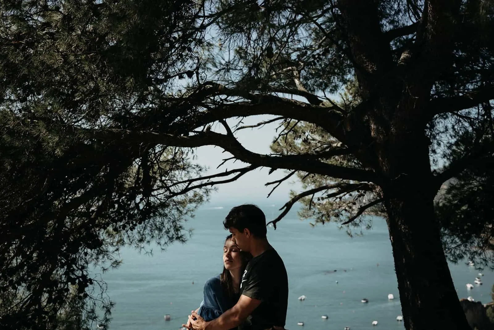 Ein Mann und eine Frau umarmen sich in der Nähe des Baumes mit Blick auf das Meer