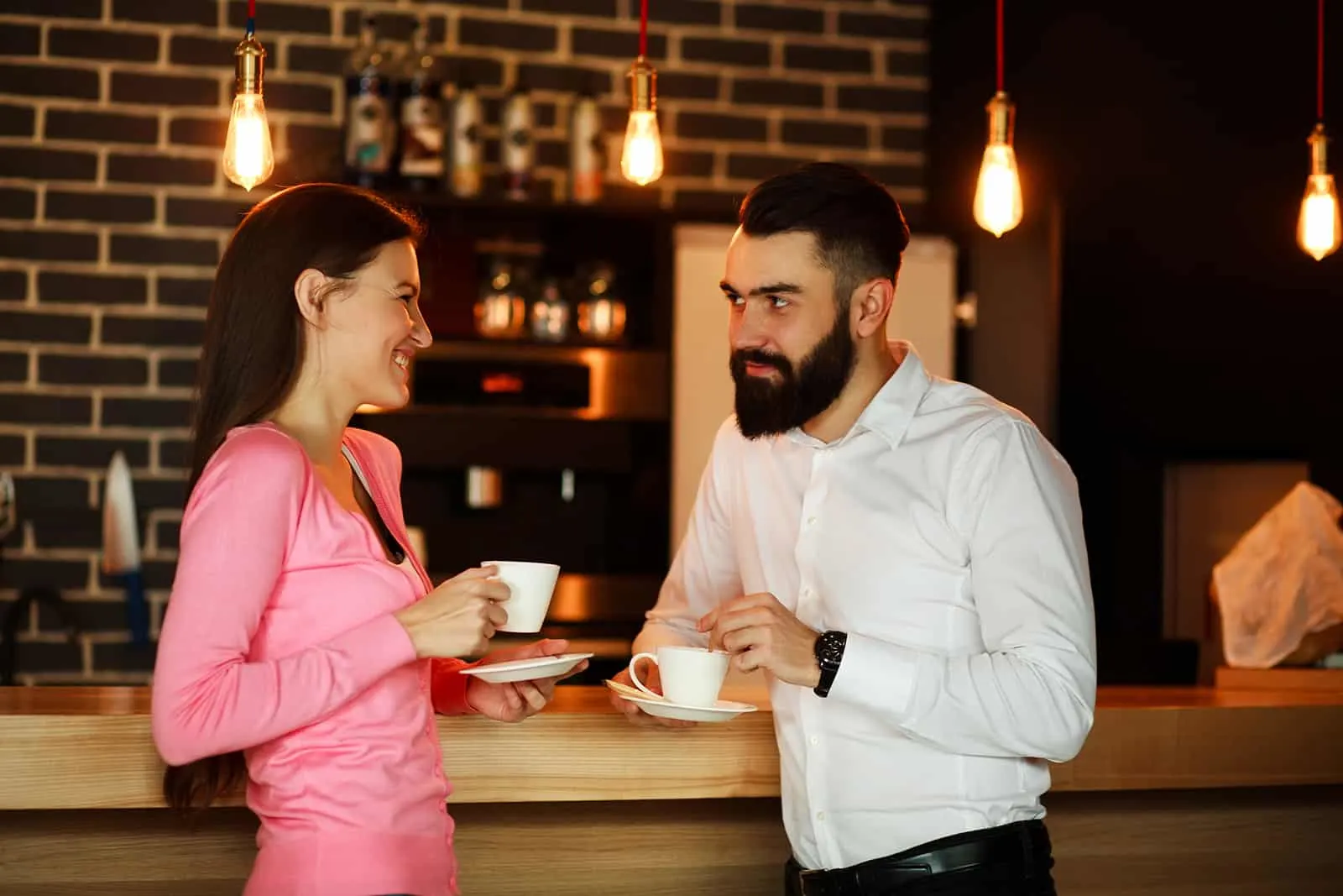 Ein lächelnder Mann und eine Frau schauen sich in die Augen und trinken Kaffee an der Theke