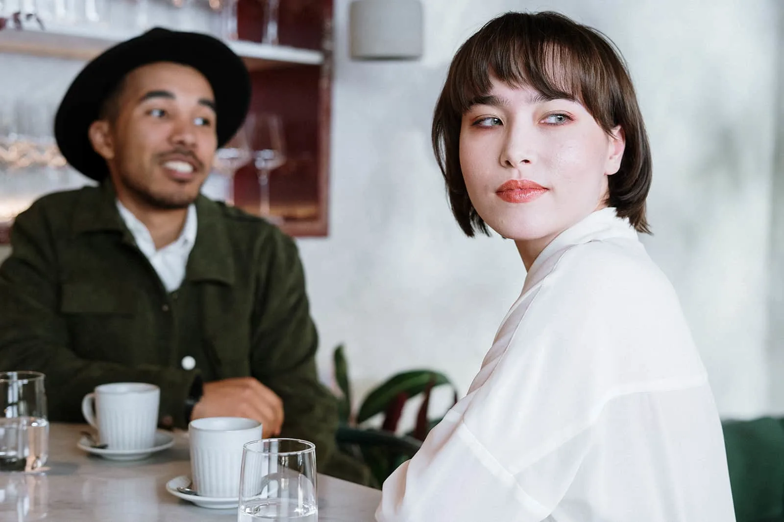 Eine Frau, die den Kopf von einem Mann dreht, der neben ihr im Café sitzt, während sie zusammen Kaffee trinkt