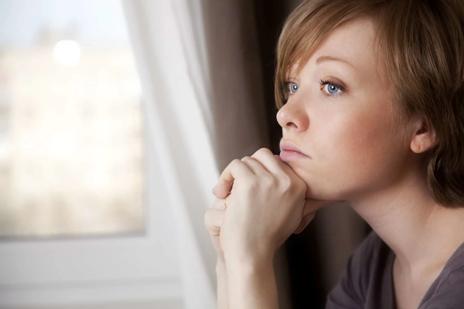 Eine kurzhaarige Frau sitzt am Fenster und denkt nach