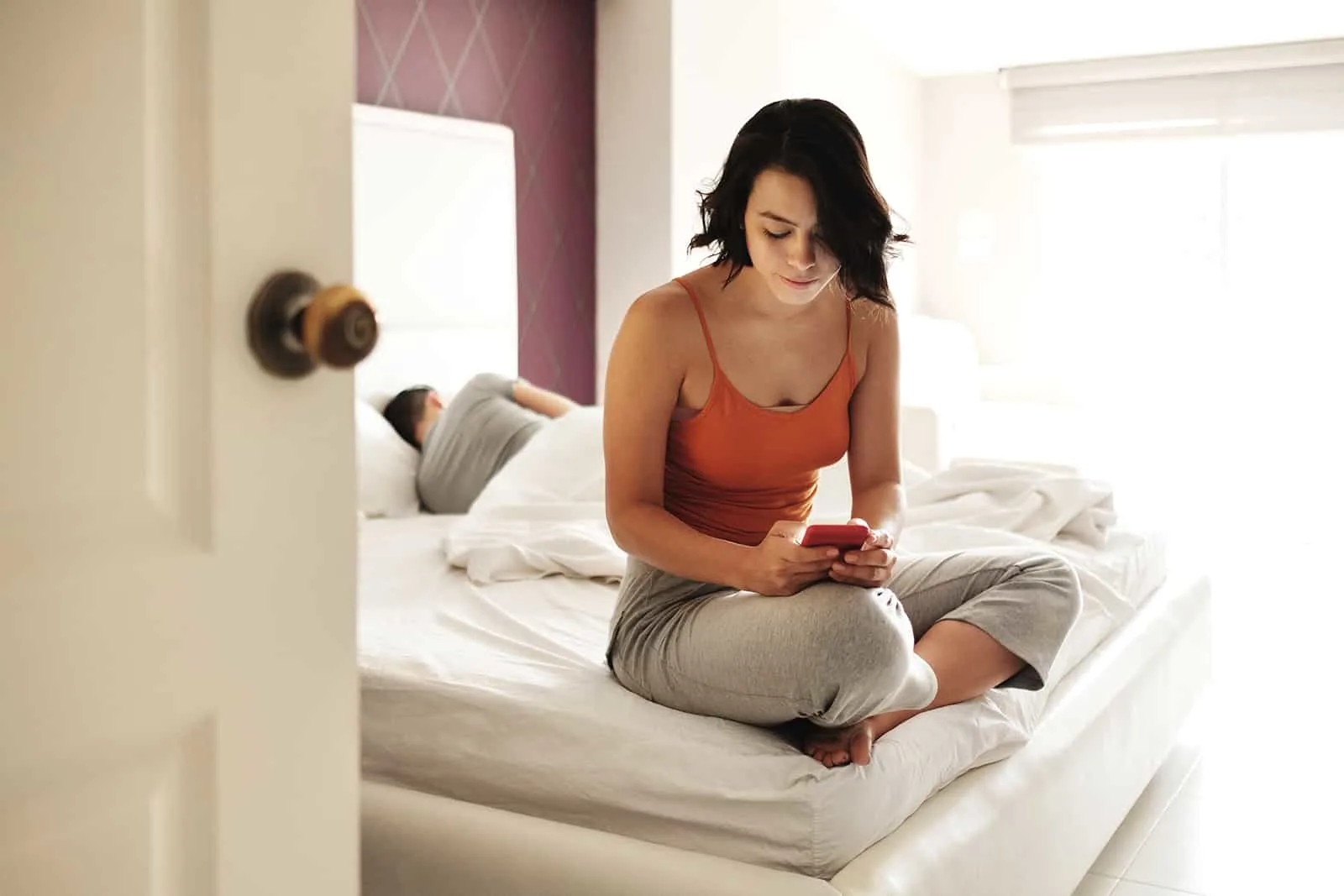 Frau SMS mit einem Smartphone, während ihr Freund im Bett liegt