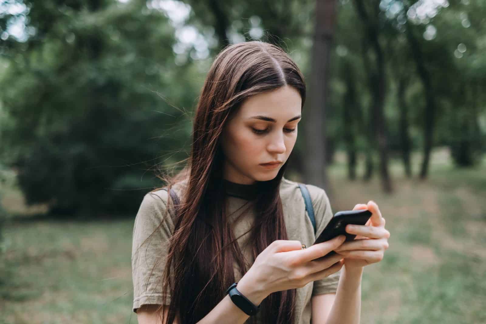 Frau allein im Stadtpark benutzt ein Smartphone