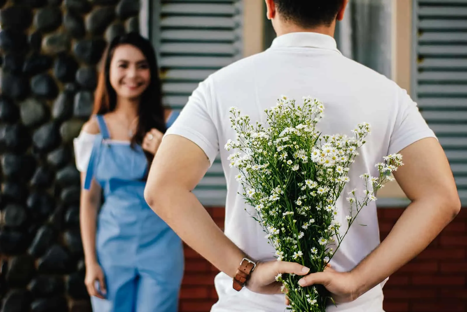 Mann, der einen Blumenstrauß hinter seinem Rücken hält, während er vor lächelnder Frau steht