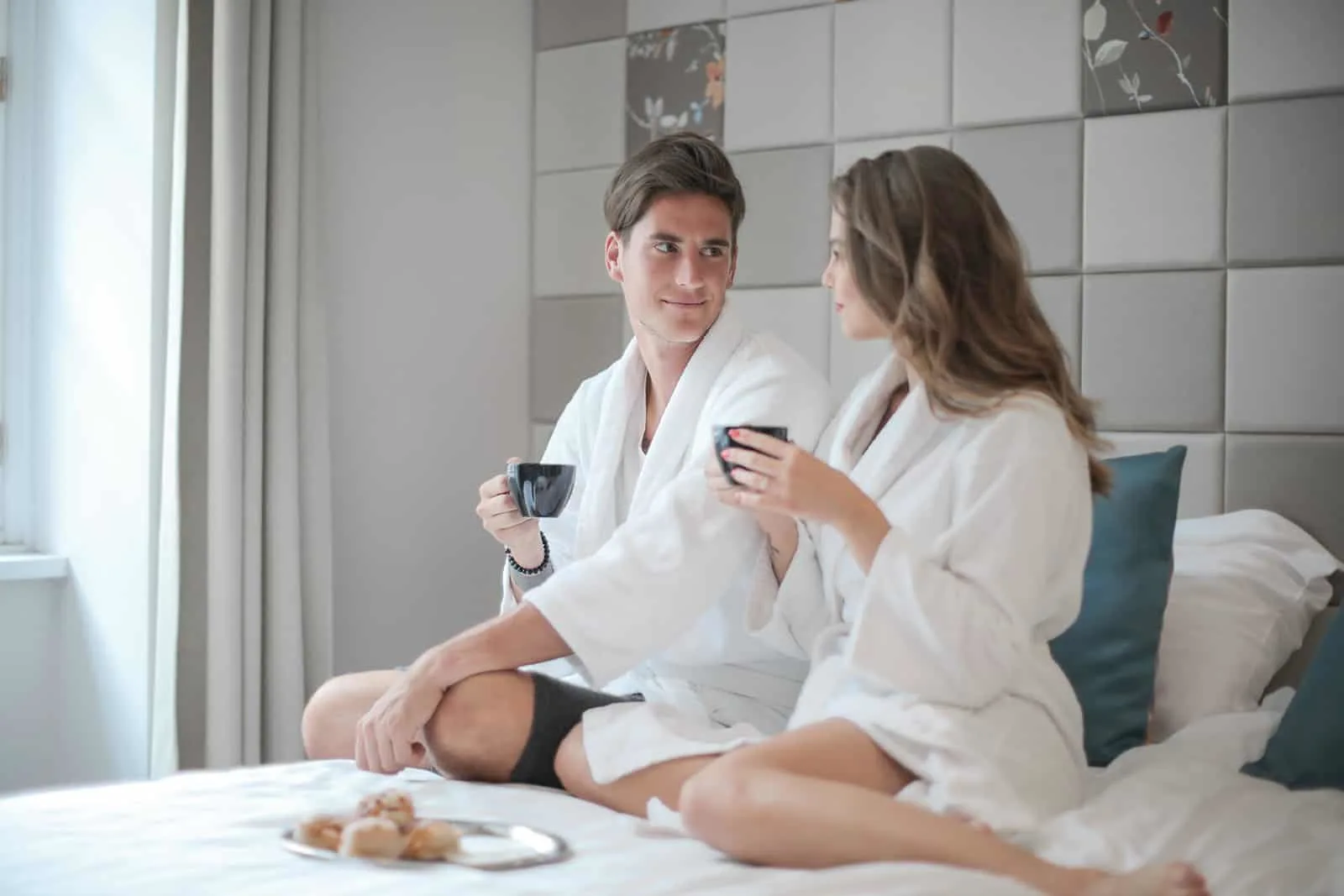 Paar sitzt auf dem Bett und trinkt Kaffee in einem Hotelzimmer