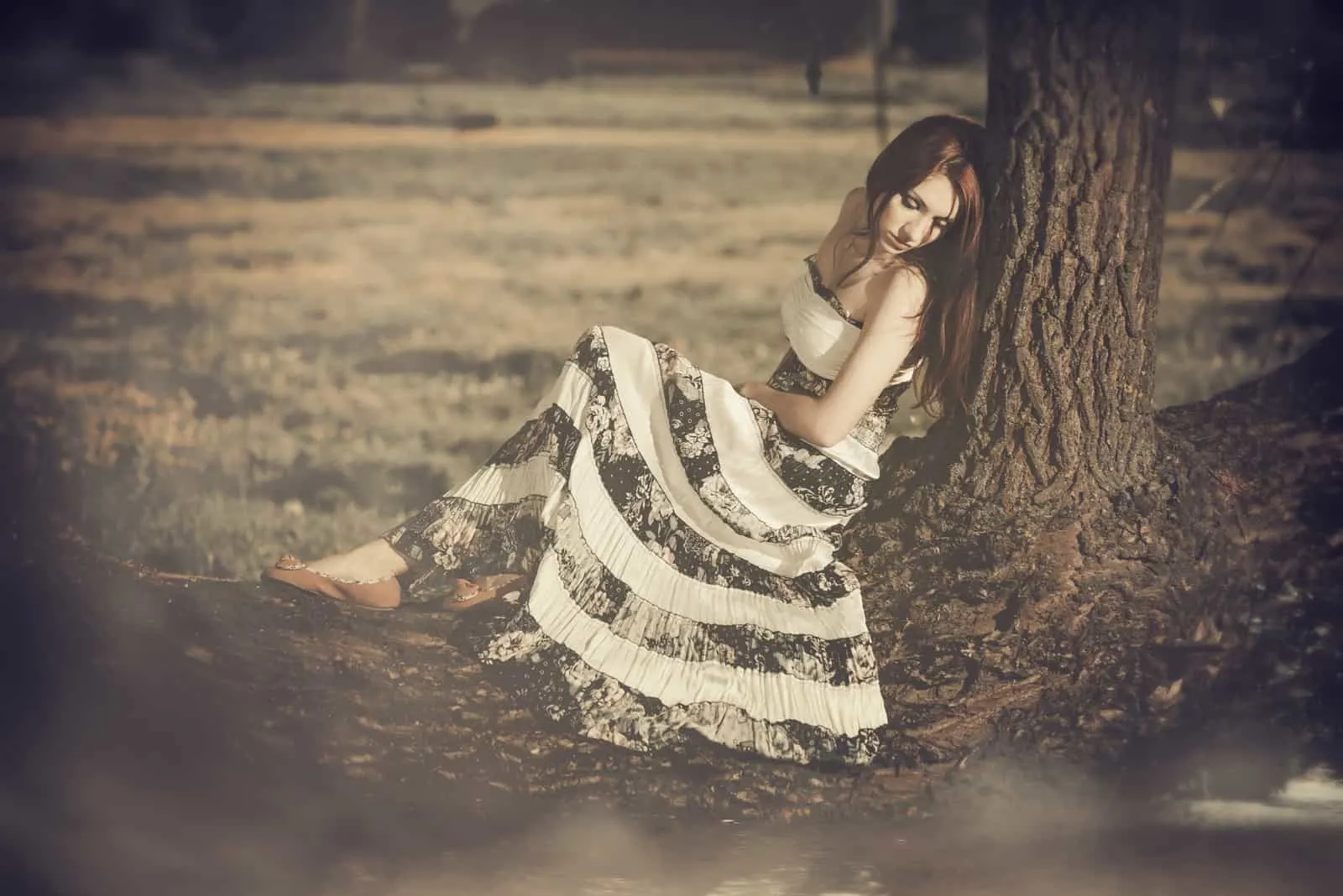 Unter dem Baum sitzt eine traurige Frau in einem schwarz-weißen Kleid